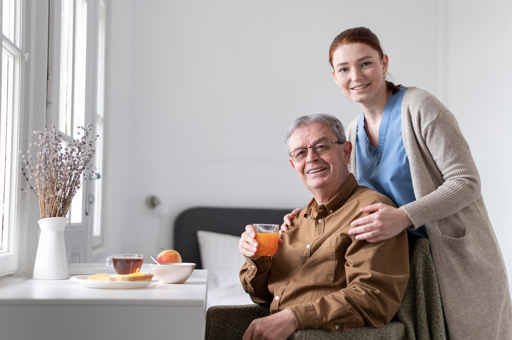 Smiling elderly man holding juice with caregiver standing beside him